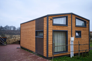 modern wooden tiny house exterior with windows, timber cladding and sleek frames on paved lot, compact modular