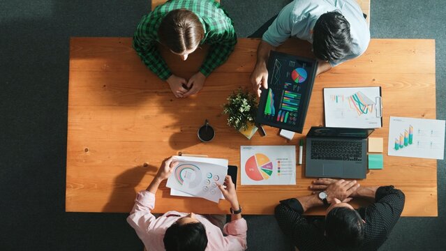 Top view of diverse business people working together to analyze chart. Top down aerial view of creative team looking at stock market report and discussing about financial investment. Convocation.
