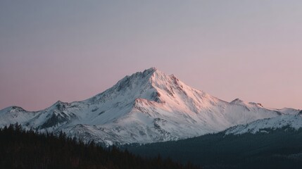 Landscape photograph of a mountain range. the mountain is covered in snow and has a jagged peak. the sky is a pale pink color, indicating that it is either sunrise or sunset.