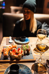 Fresh sushi platter and white wine on a wooden table with a woman dining in a cozy Japanese restaurant