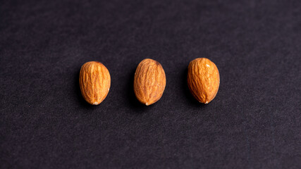 Three almonds are placed in a row on a black surface