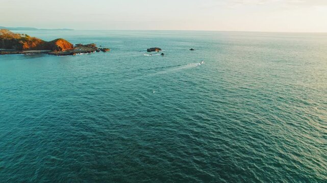 Boat speeding through calm turquoise sea near rocky coast at sunset Costa Rica