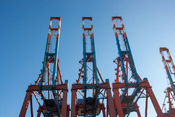 Three massive red container cranes standing tall against a clear blue sky in the busy Port of Hamburg