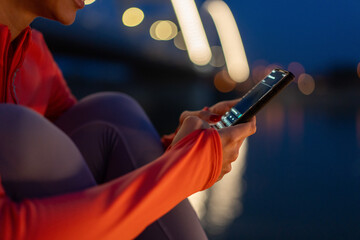 Woman using smartphone outdoors at night with blurred lights in background