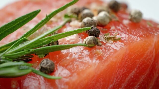 A vibrant close-up shot captures the exquisite detail of a fresh piece of uncooked fish, richly textured and gleaming with natural oils. Sprigs of fragrant rosemary and a medley of whole peppercorns a