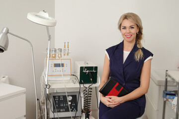 Smiling beautician sitting with notebook in beauty clinic
