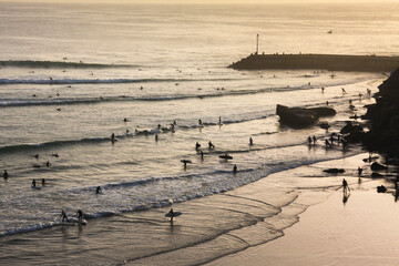 High-angle view of Magic Bay in Imsouane, Morocco, showing a crowd of surfers in the ocean and walking along the beach