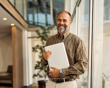 Portrait of a smart inteligent senior businessman holding a laptop computer in office