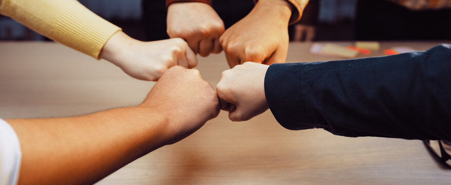 A group of diverse individuals showcases teamwork through a fist bump gesture, symbolizing unity and support in a collaborative office environment. SACTR
