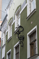 A close-up view of a green building facade with white trim and windows, featuring a decorative black wrought-iron sign shaped like a dragon in Riga, Latvia