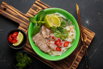 Vietnamese pho bo noodle soup beef lime asian bowl dinner black background wooden cutting board