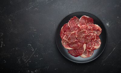 Raw marbled thin beef slices carpaccio black plate preparing cooking top view copy space
