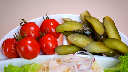 Set of chopped fermented pickles, tomatoes and sauerkraut decorated with greenery and red onion in clay brown bowl. Collection of homemade salty appetisers made of vegetables placed on straw stand.