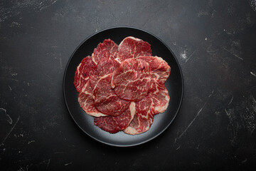 Raw marbled thin beef slices carpaccio black plate preparing cooking top view