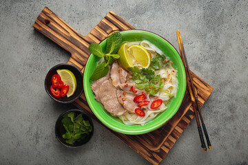 Vietnamese pho bo noodle soup beef lime asian bowl dinner gray background wooden cutting board
