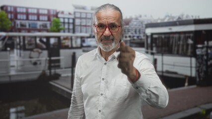 Man with long hair and beard points finger at camera on amsterdam canal street; determination warning.