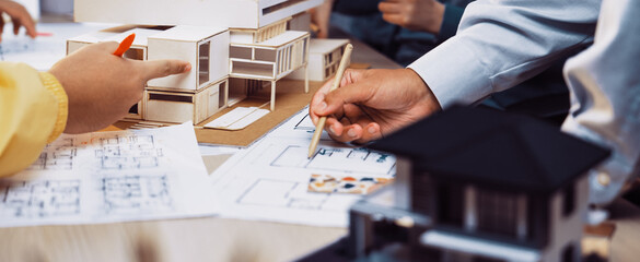 A vibrant architecture studio scene showing professionals engaged in model building and discussion. Various design sketches and physical models illustrate creative processes and teamwork. SACTR