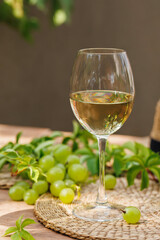 Single glass of white wine with fresh green grapes and vine leaves on a wooden table outdoors