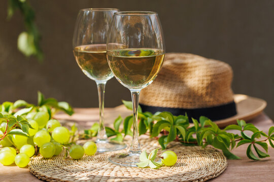 Two white wine glasses with bunch of grapes and leafy vines on rustic summer table..