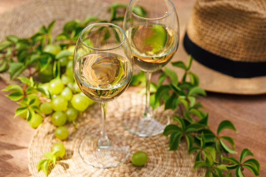 Two glasses of white wine with green grapes and fresh vines on sunlit outdoor table..