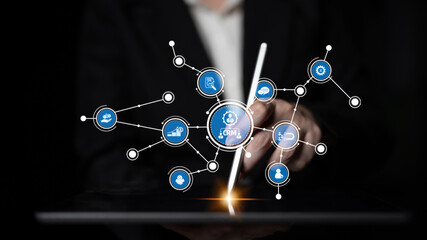 A person interacts with a digital tablet showcasing abstract CRM data connections and graphical icons in a dark environment, symbolizing modern technology and business integration. Tessel
