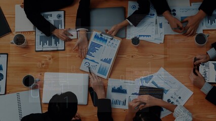 Overhead view of a collaborative business meeting. Professionals analyze charts and data on a wooden table, engaging in strategic discussions to drive success. Raster