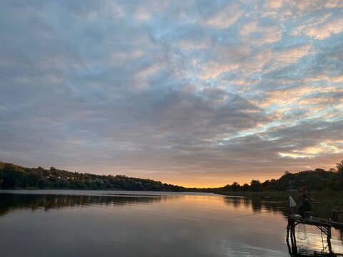 Fisherman waits on pier under dramatic glowing evening sky