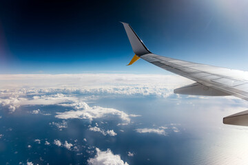 Fototapeta premium Airplane wing extending over a vast ocean, with fluffy clouds scattered below, showcasing the beauty of flight and the expansive sky above, perfect for travel themes