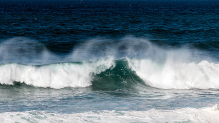 Powerful ocean waves crashing against the shore, creating a misty spray, with deep blue water and white foam, capturing the beauty of nature's force and tranquility