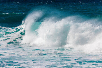 Powerful ocean waves crashing against the shore create a stunning display of nature's force, with foamy white surf contrasting against deep blue water and a clear sky above