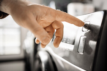 Close-up of a hand pressing the start button on a modern washing machine, showcasing sleek design and functionality in a contemporary laundry room environment