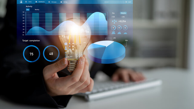 A business professional engages in data analysis while holding a light bulb, symbolizing innovation. The digital graphs and charts in the background illustrate key insights and trends. Impute