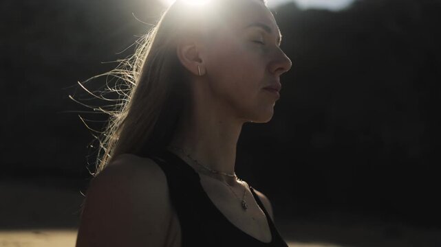 Close-up face portrait of healthy woman meditating with closed eyes on a dark background with sun rays, mental health, meditation, yoga, tantra, mantra, spirituality, sports, breathing, hope, healing