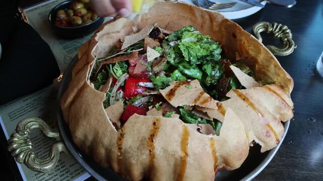 fancy elaborate fattoush salad inside a fried crispy pita bread shell being broken before eating with a spoon (middle eastern lebanese israeli syrian appetizer with pomegranate molasses and seeds)
