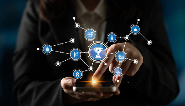 A businesswoman in a suit interacts with a smartphone displaying digital icons that symbolize achievement and success, reflecting modern technology and connectivity. Tessel - Powered by Adobe