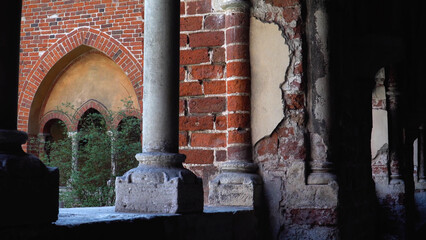 View of Riga Cathedral’s (Latvia) red brick facade framed by shaded corridor arches, blending Romanesque, Gothic, Baroque, and Art Nouveau styles.