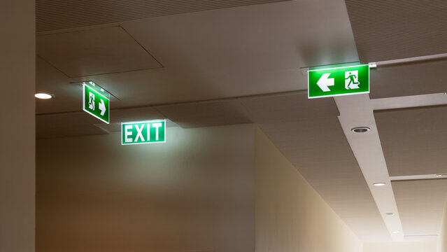 A green fire escape sign hangs from the ceiling, showing an exit sign green light box with a running man and an arrow pointing right for safety and evacuation.