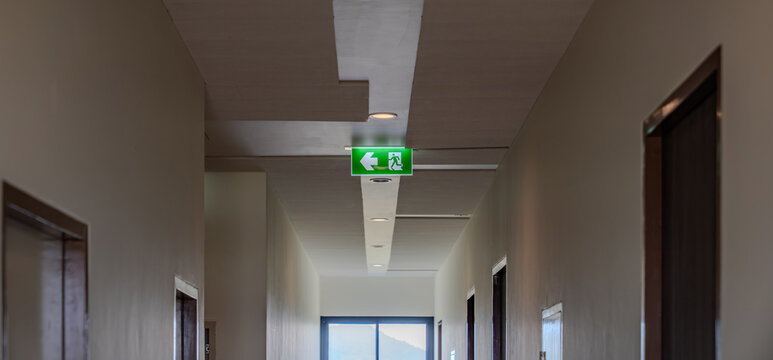 A green fire escape sign hangs from the ceiling, showing an exit sign green light box with a running man and an arrow pointing right for safety and evacuation.