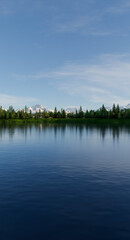Serene Lake Scene With Pine Forest, Snowy Mountains, And Clear Blue Sky Reflections