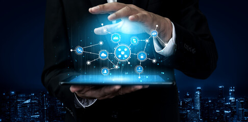 A businessman in a suit holds a tablet showcasing dynamic digital connections and data visualizations against a sleek night cityscape, symbolizing innovation and technology. Tessel