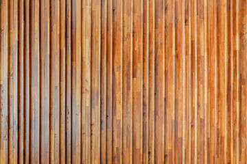 A wall made of vertical wooden planks in various brown tones shows natural grain lines texture variations and visible seams between each plank.