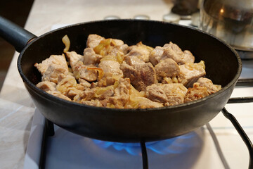 Frying meat. Pieces of meat with onion in frying pan on gas stove