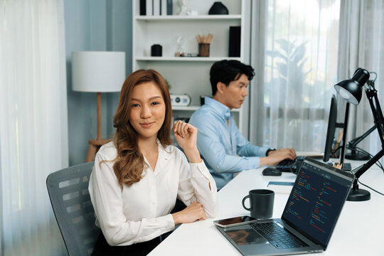 Profile smiling beautiful Asian businesswoman looking camera to portrait pose at modern office on working desk casual day. Blurry background man colleague analyzing data market plan on pc. Infobahn.