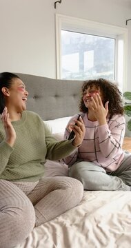 Vertical video: Female friends in bed adjusting eye patches testing AR filter with phone, laughing
