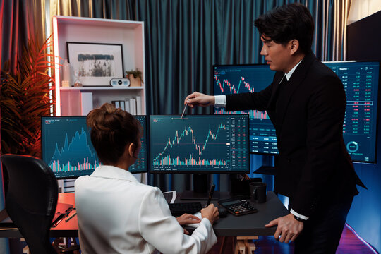 Trading business partners discussing on dynamic stock exchange statistic on pc screens taking note on paper, comparing with high or low point on currency graph at night neon modern office. Infobahn. - Powered by Adobe