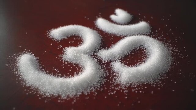 The sacred Om symbol created with white sugar granules on a dark red surface representing spirituality and purity.
