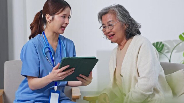 Asian compassionate elderly care nurse showing tablet to smiling senior woman cozy living room setting with soft natural light and supportive interaction young nurse showing tablet to elderly woman