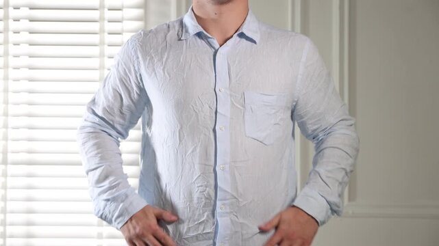 Man putting on creased shirt indoors, closeup