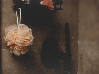 Soft bath sponge hanging in a shower with water droplets on a glass. A peach-colored bath sponge hangs in a shower, with water droplets on the glass. Modern bathroom interior. Spa day, daily routine.
