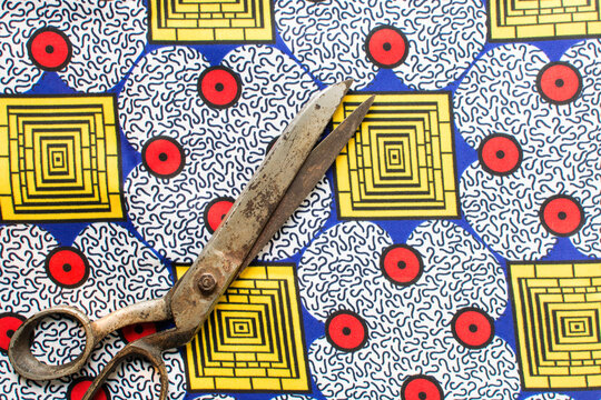Top view of tarnished silver scissors on ankara fabric, large antique tailor scissors and ankara material on a table